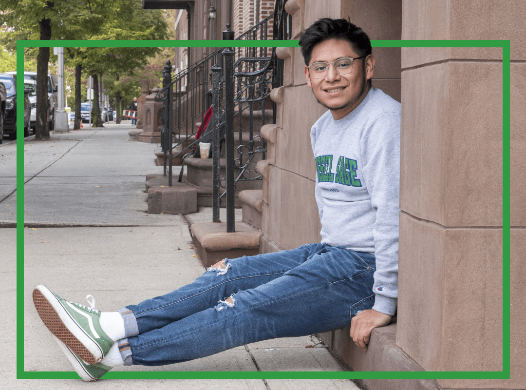 A student sitting on a sidewalk in town.